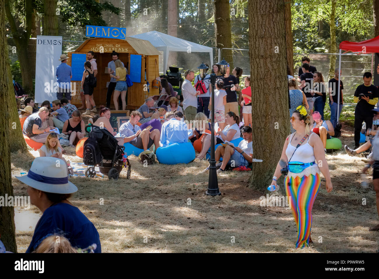 Frau wandern in gestreiften Leggings mit Blumen im Haar, eine Flasche Wasser und eine Kamera, und die Menschen, die an verschiedenen Zelte, Includin Stockfoto