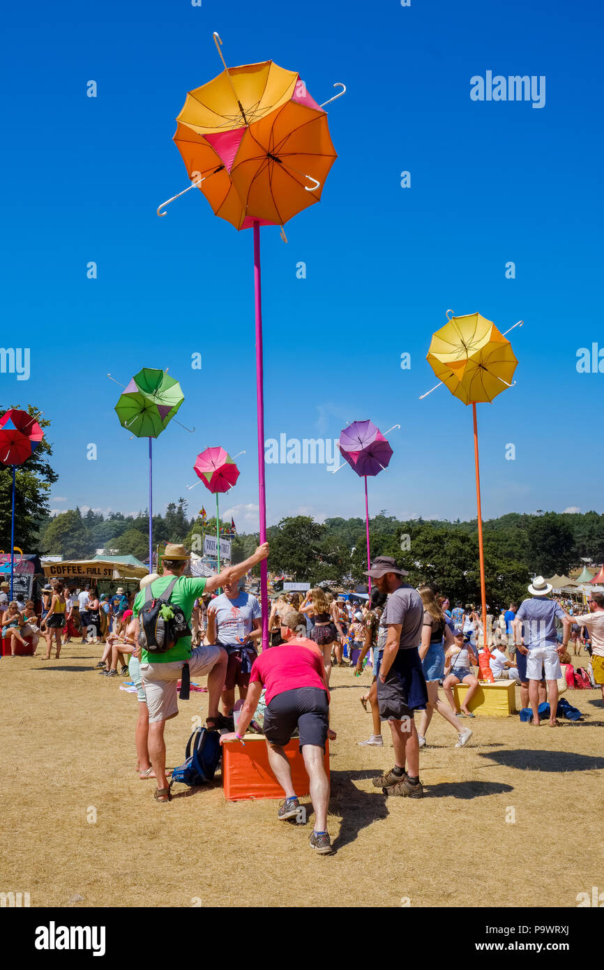 Der Mensch macht Dehnübungen als weiteres der Ständer hält mit bunten Schirme als Fake Blumen, während andere Leute stehen, sitzen, Wandern aroun Stockfoto