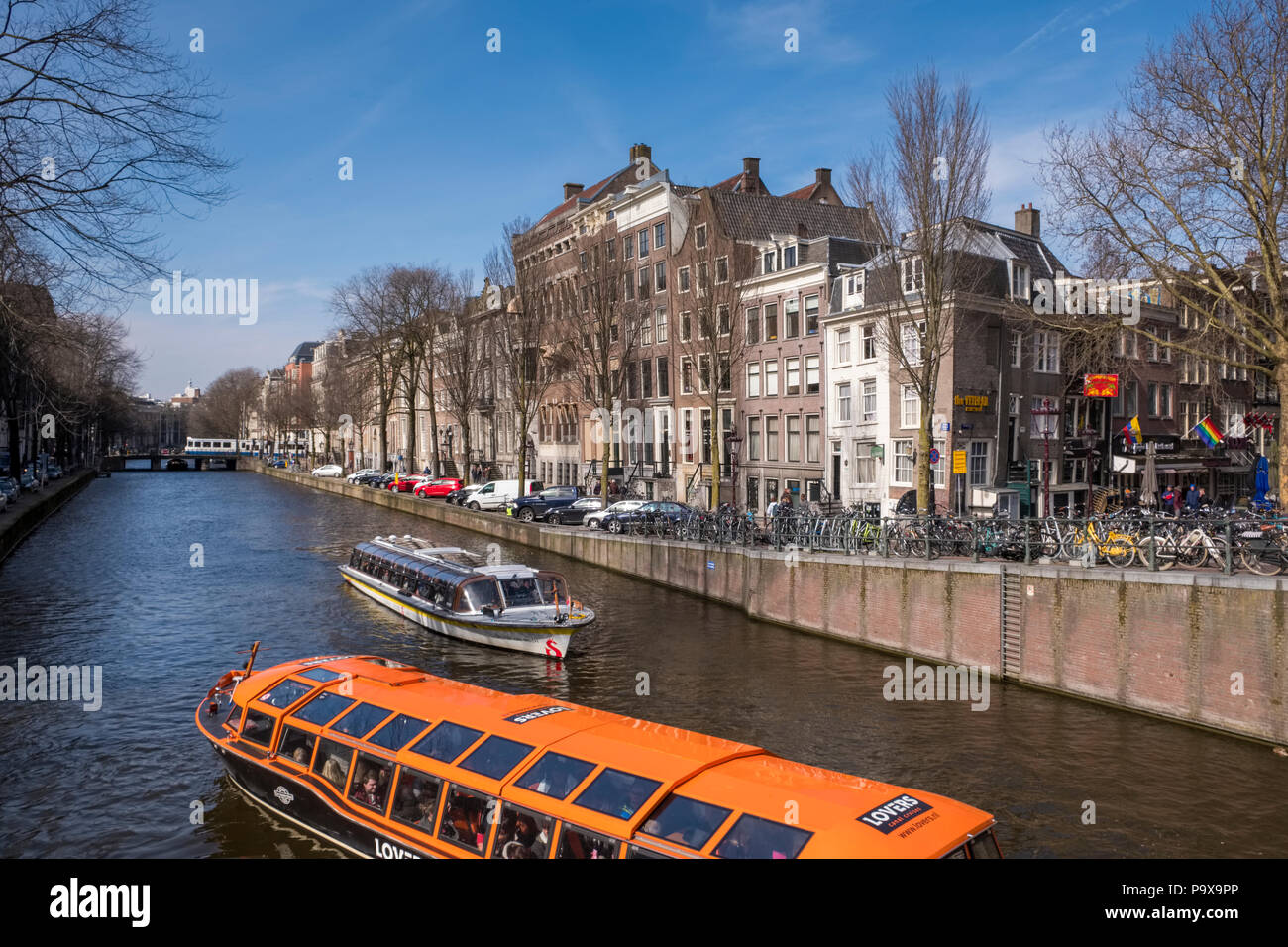 Dünne Grachtenhäuser und Sightseeing Boote auf touristische Kreuzfahrten auf einem Kanal in Amsterdam, Niederlande, Europa Stockfoto