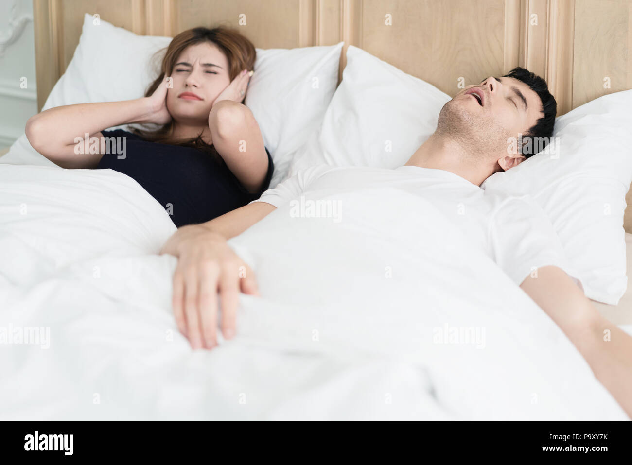 Verärgert asiatische Frau blockieren Ihre Ohren vor Lärm von Mann Schnarchen im Schlafzimmer zu Hause. Junge Paare haben Probleme mit dem Schnarchen. Stockfoto