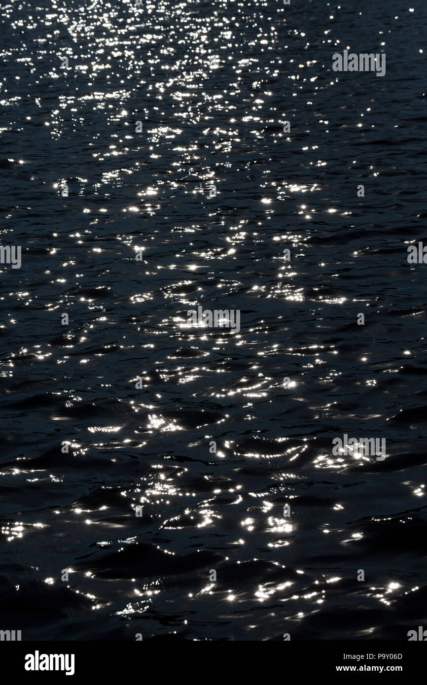 Schwarz Zusammenfassung Hintergrund der dunklen Wasser in einem See und weiße Sonne Spiegelungen auf der Oberfläche der Wellen, unscharf Stockfoto