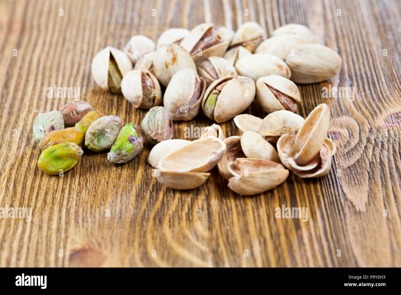 Chaotisch verstreut und auf einem hölzernen Tisch gestapelt, reife geröstete Pistazien, close-up. Ein Teil der Nüsse sind gereinigt und liegen in einem separaten Heap, gerade Stockfoto