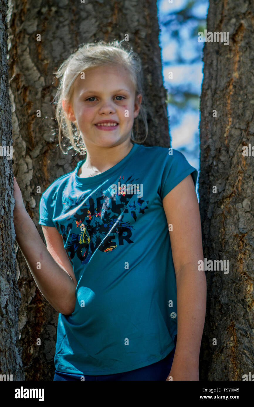 Hübsches blondes Mädchen, im Baseball Hut und blauen Outfit, smiljng an Kamera, wie sie im Schatten der Baum sitzt. Model Release #113 Stockfoto