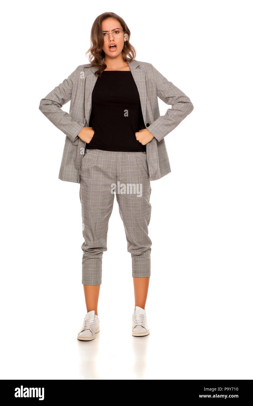 Wütende junge schöne Frau in einer Jacke, Bluse, Hose, Turnschuhe und Gläser Stockfoto