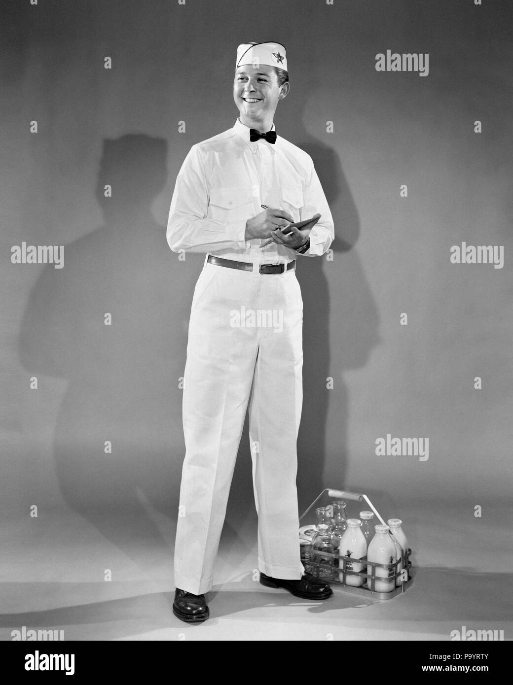 1940er Jahre 1950er Jahre LÄCHELN HOME DELIVERY MILCHMANN NEBEN FLASCHEN MILCH MIT STIFT UND NOTIZBLOCK - aspy 5367 ASP001 HARS junger Erwachsener GERNE FREUDE JOBS STUDIO SHOT CARRIER MOLKEREI IN VOLLER LÄNGE PERSONEN MÄNNER BERUF NÄCHSTE B&W LIEFERN BESETZUNG FREUNDLICHEN KUNDENSERVICE UND MILCHMANN STOLZ ZU BERUFEN LÄCHELT FRÖHLICH BOW TIE MILCH FLASCHE MILCH MANN junger erwachsener Mann SCHWARZ UND WEISS KAUKASISCHEN ETHNIE ALTMODISCH Stockfoto