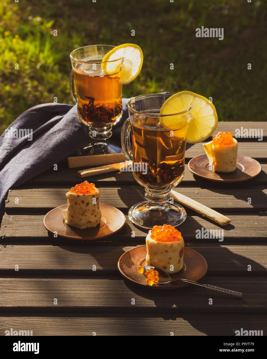 Pfannkuchen mit roter Kaviar, zwei Gläser mit Tee und Scheiben von Zitronen. Abendsonne Stockfoto