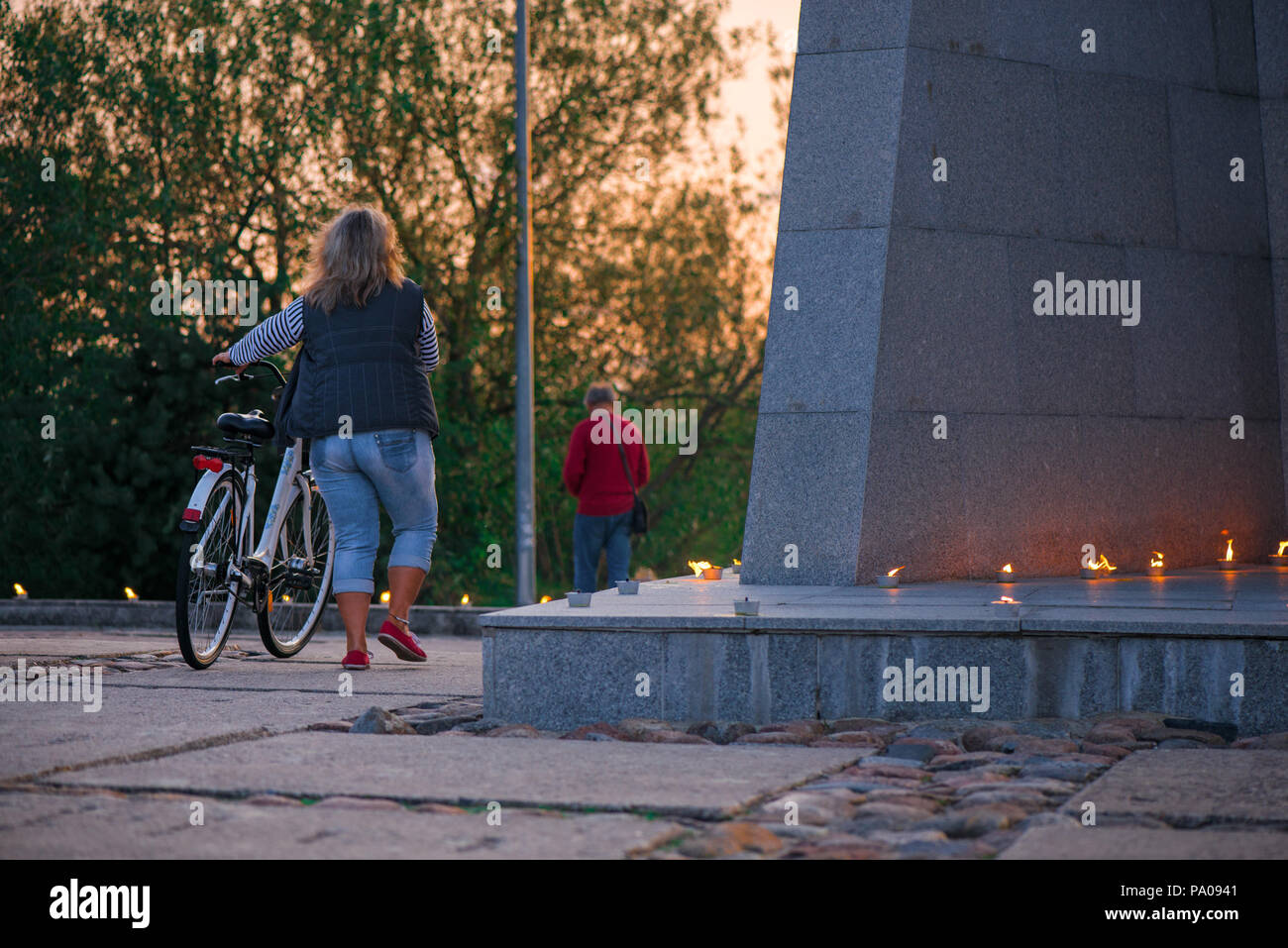 Frau mit Fahrrad Wandern im Park. Romantische Lagerfeuer Nacht am Meer bei Sonnenuntergang. Leute versammeln um Nacht der alten Leuchten feiern Stockfoto