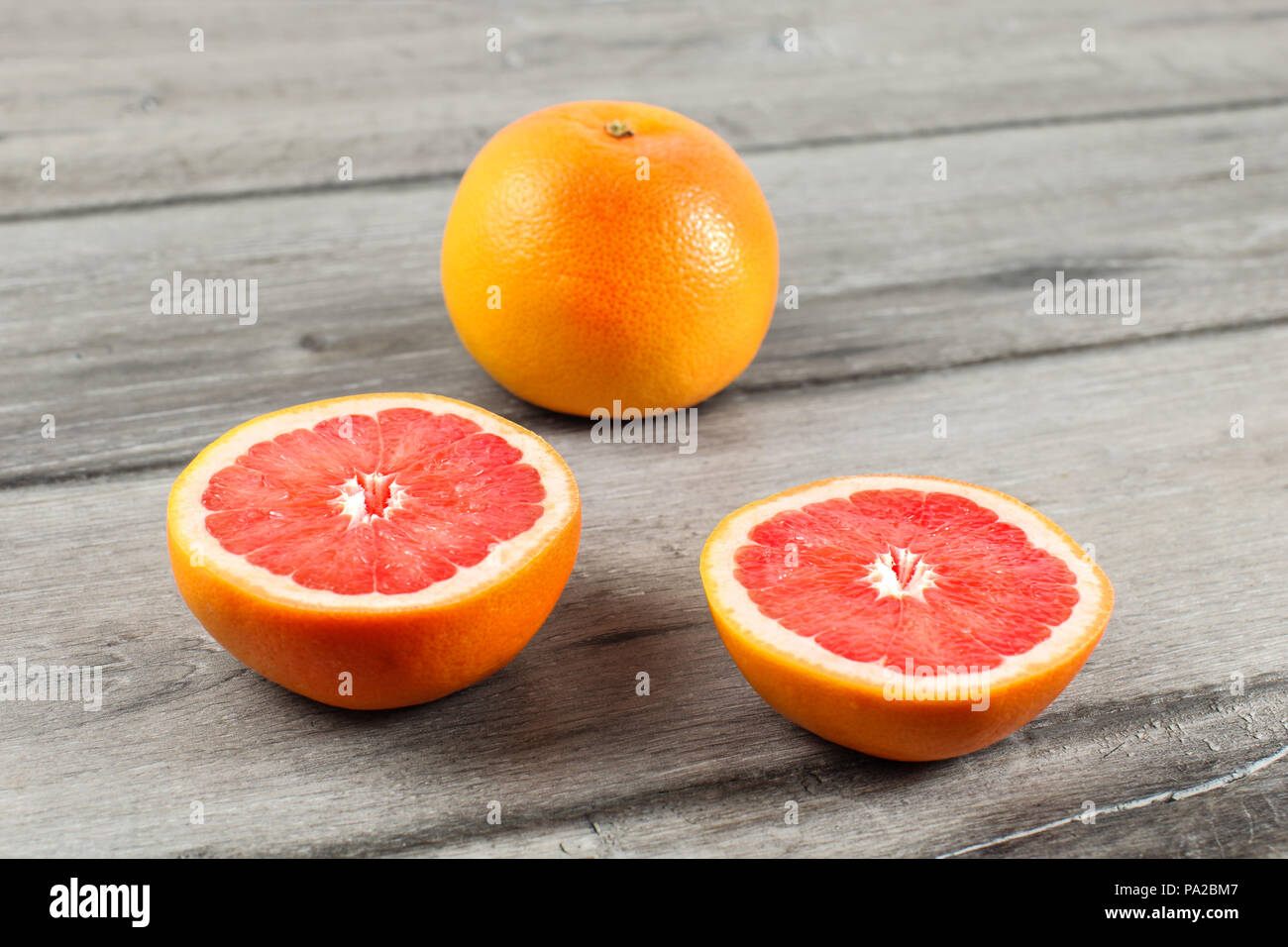 Rosa grapefruit Schnitt zu Hälfte, mit anderen Zitrusfrüchten im Hintergrund, auf grau Holz Tisch platziert. Stockfoto