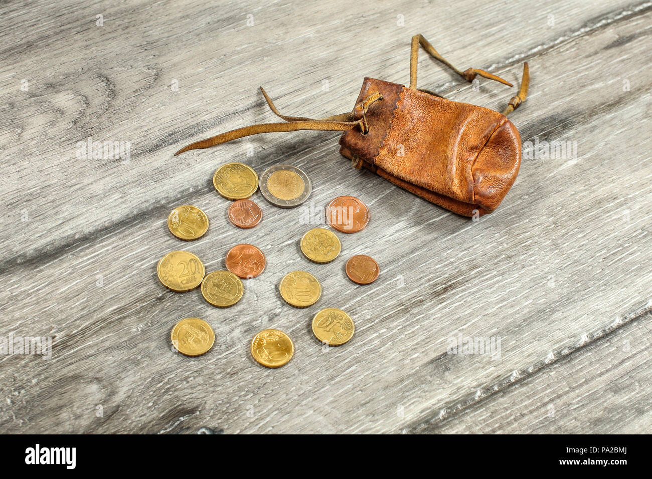Alte abgenutzte Münze aus braunem Leder Tasche, mit Euro-münzen auf grau Holz Schreibtisch verschüttet. Stockfoto