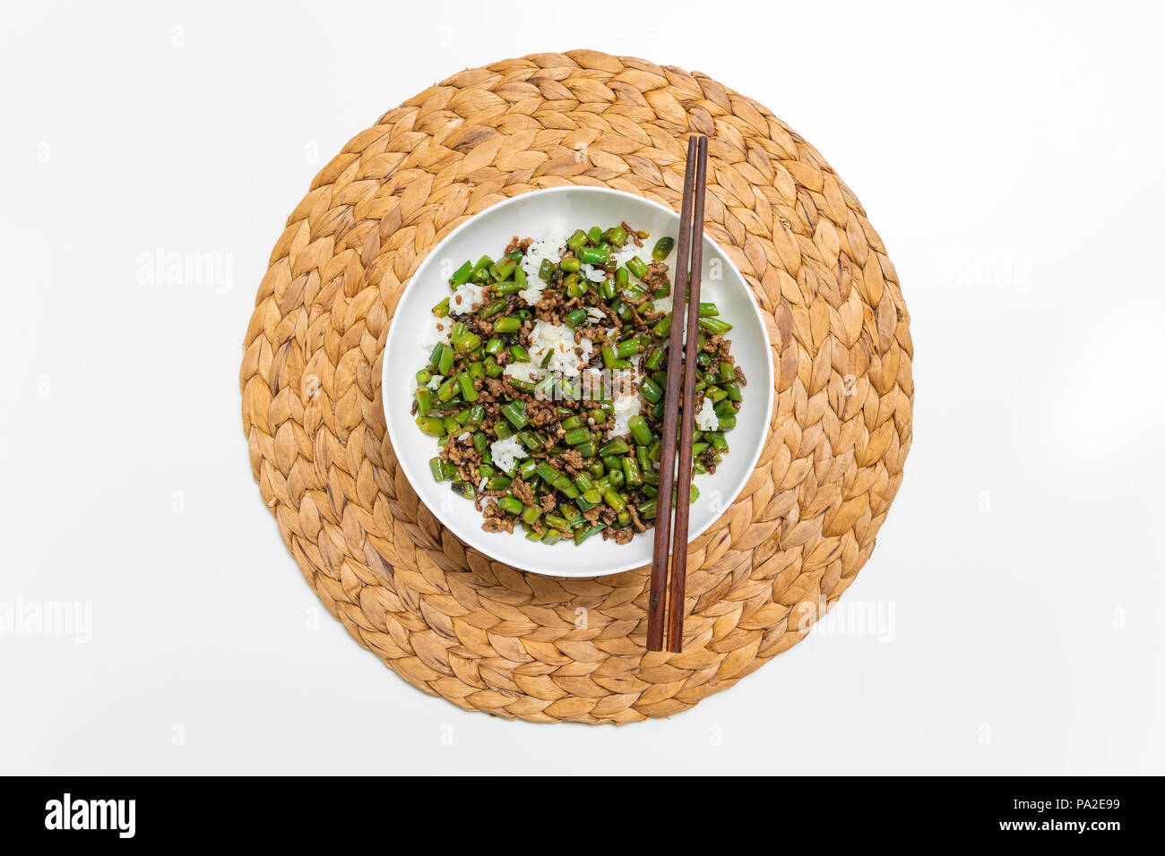 Schüssel mit Hackfleisch Eintopf mit Bohnen serviert über gekochten Reis mit Essstäbchen auf einem runden Strohmatte Stockfoto