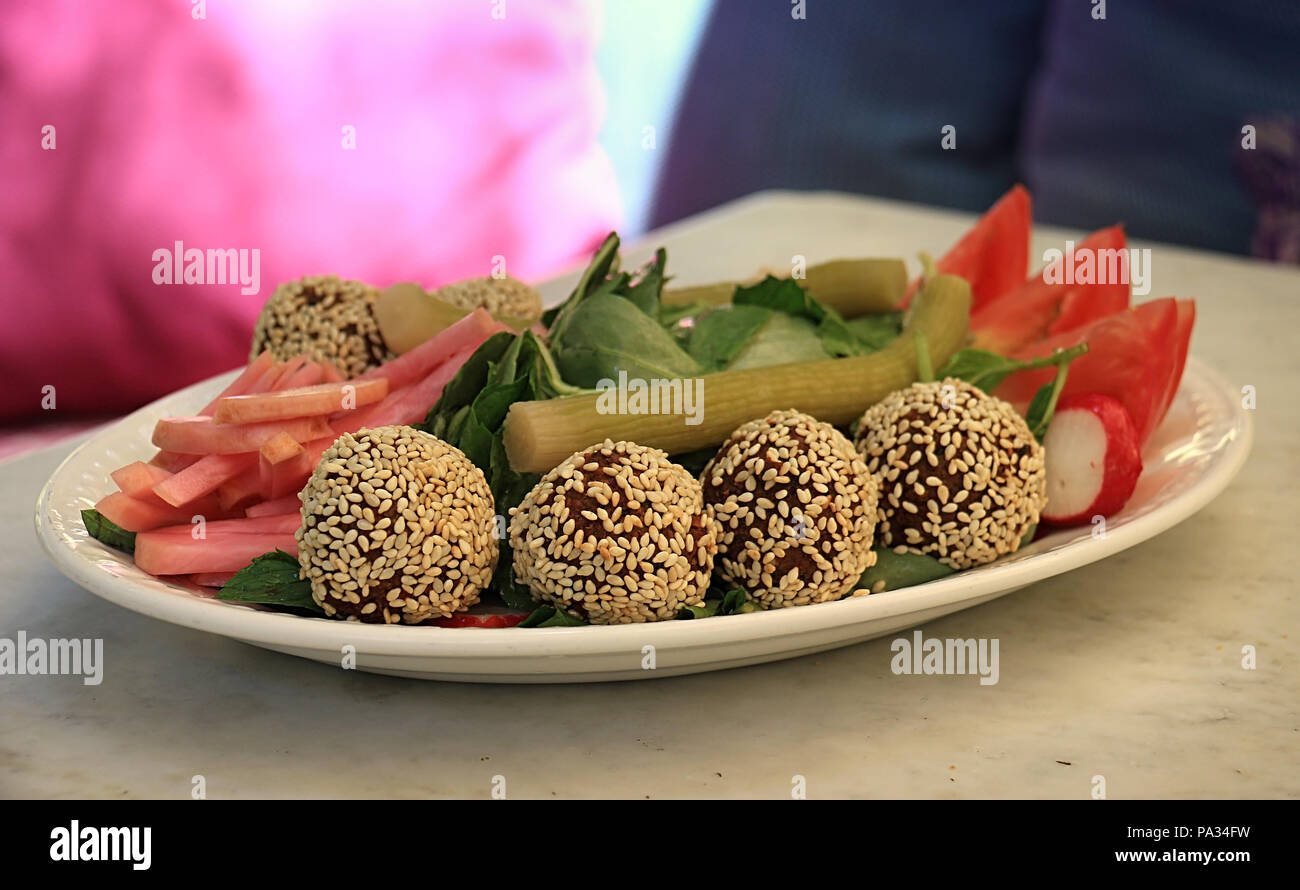 Falafelkugeln in Sesam in einer Schüssel zusammen mit der traditionellen begleitenden Gemüse abgedeckt. Stockfoto