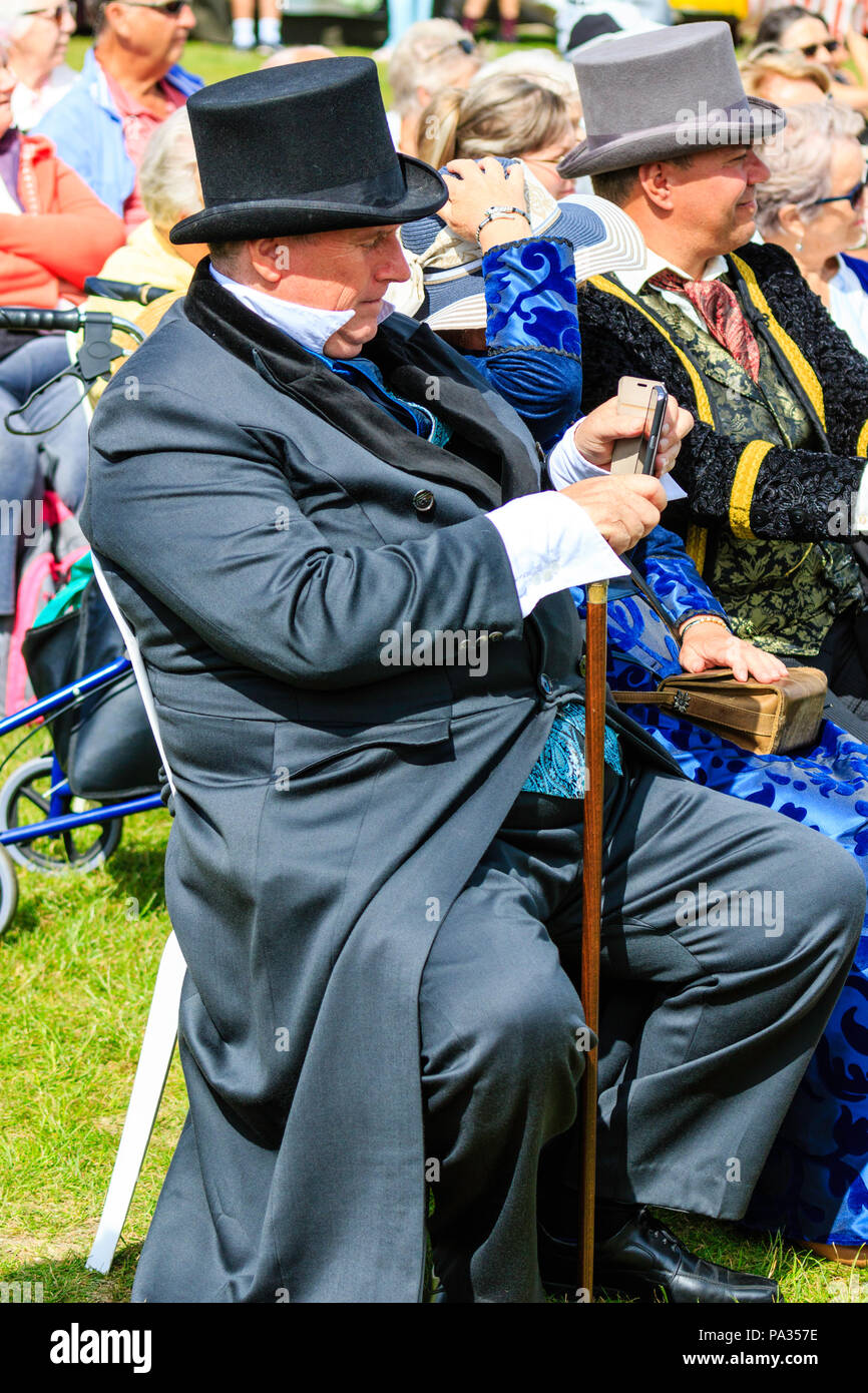 Älterer Mann mit viktorianischen Oberschicht Kleidung, Sitzen im Freien mit Anderen. Holding und Handy. Charles Dickens Festival. Stockfoto