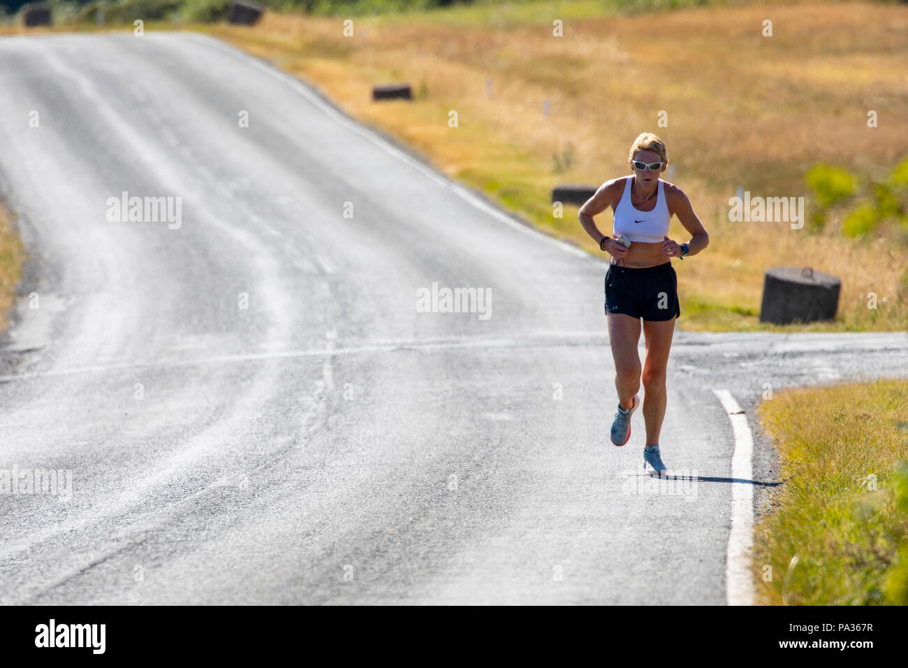 Eine weibliche Road Runner in Hot Waliser Sonnenschein während einer Hitzewelle in Nord Wales, Großbritannien läuft Stockfoto