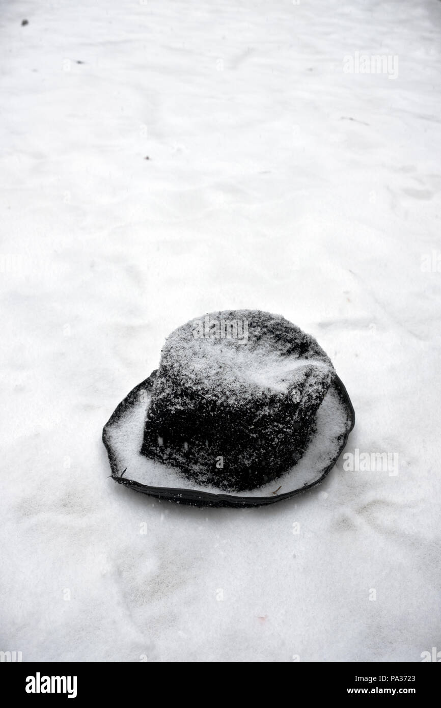 Eine alte zerschlagen schwarz Filz Hut im Schnee langsam durch den frischen Schnee im Winter abgedeckt werden liegt Stockfoto