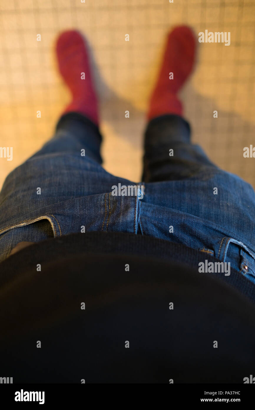 Selfie Ansehen der Fotograf schaut auf seine untere Hälfte, einschließlich, Bauch mit schwarzem Jersey, Jeans und roten winter Socken auf gefliestem Boden Stockfoto