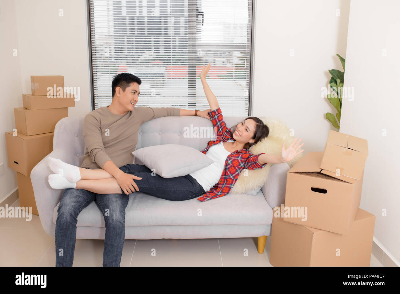 Glückliches Paar entspannt auf einem Sofa, das Spaß am Umzugstag, neugierige junge Hausbesitzer genießen Umzug in ein neues Zuhause, positive lachenden Mann und Frau Stockfoto