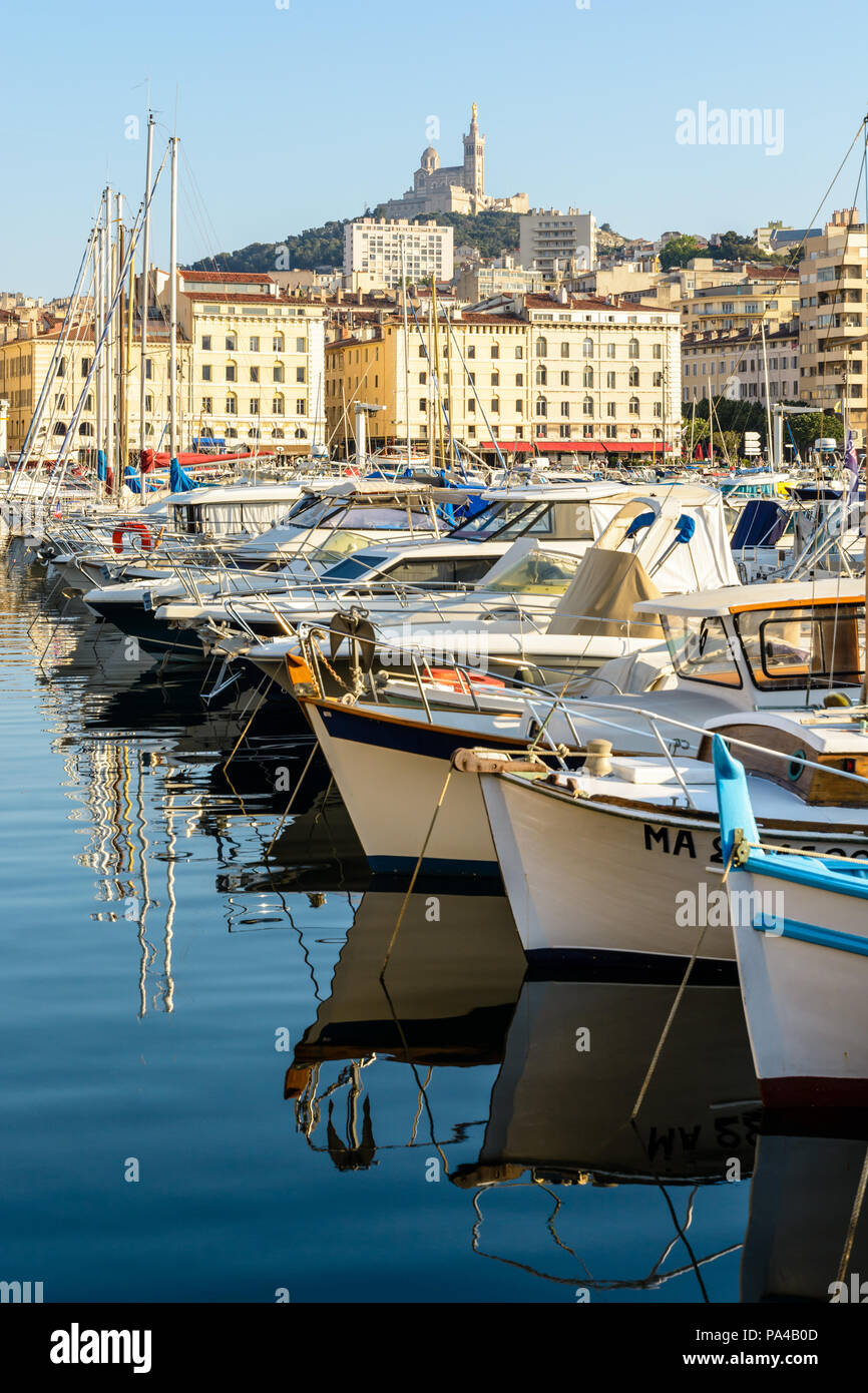 Der alte Hafen von Marseille, Frankreich, bei Sonnenuntergang mit Boote im Wasser widerspiegelt und der Basilika Notre-Dame de la Garde auf der Spitze des Hügels. Stockfoto