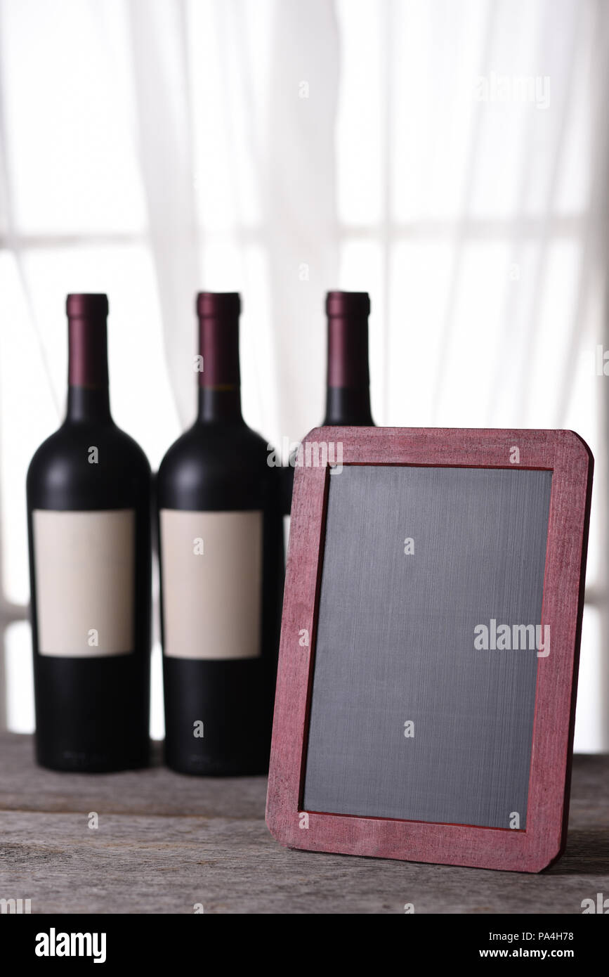 Drei Flaschen Rotwein hinter eine leere Schiefertafel bereit für Ihre Kopie. Perfekt für eine Weinkarte oder Weinverkostung. Stockfoto