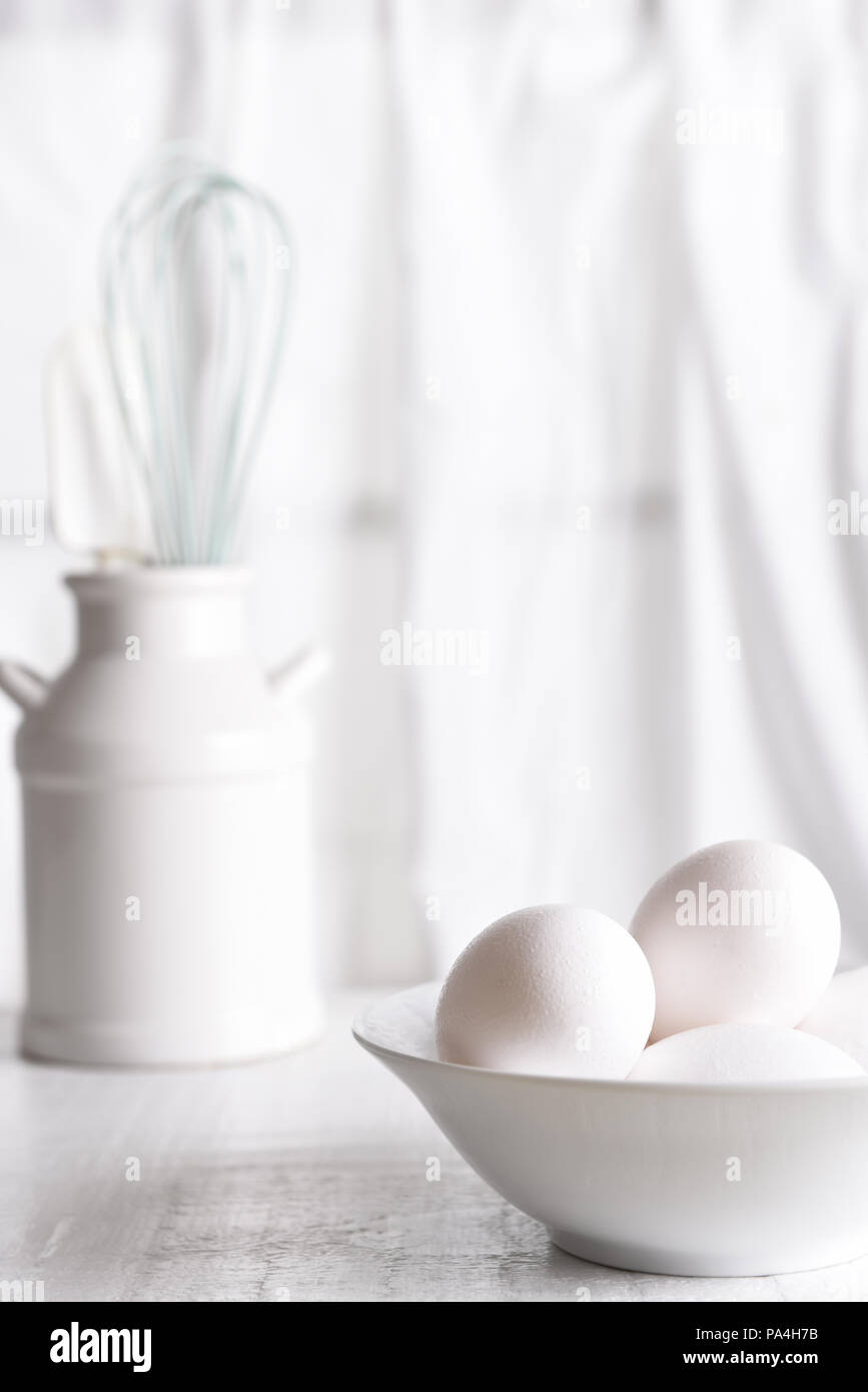 High Key Ei noch Leben: frische Eier in einer weißen Schüssel vor einem Fenster mit weißen Vorhängen. Vertikale Ausrichtung. Stockfoto