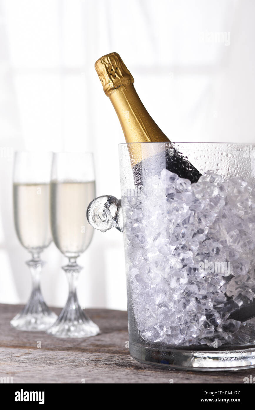 Eine Flasche Champagner in einem Eiskübel vor ein Fenster mit zwei Flöten im Hintergrund. Stockfoto