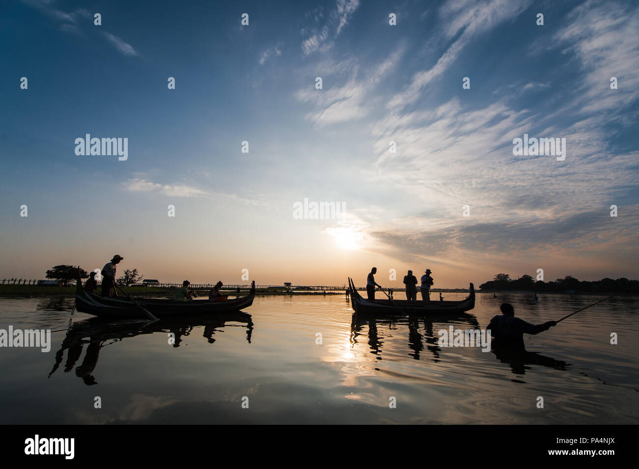 Boote mit Touristen auf dem Taung Tha Mann See mit der U-Bein Brücke im Hintergrund, während ein Sonnenuntergang in Mandalay, Myanmar Stockfoto