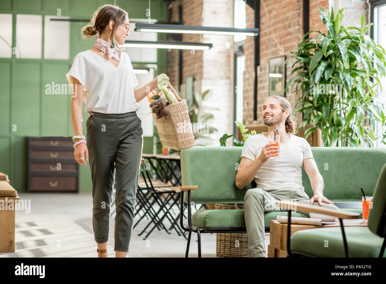 Frau gehen durch den Mann auf dem Sofa in der schönen grünen Innenbereich sitzen Stockfoto