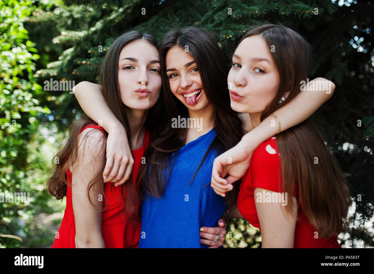 Drei jugendliche Mädchen in Blau und rote Kleider, Outdoor und zeigt tonque. Stockfoto