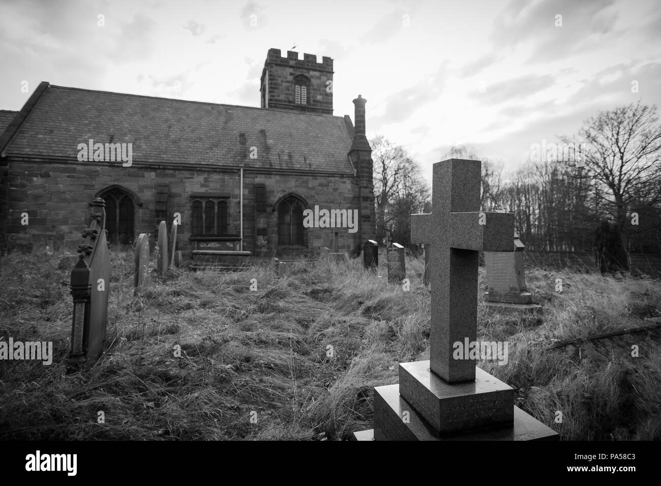 Schwarze und weiße Kruzifix mit Kirche und Friedhof im Hintergrund Stockfoto