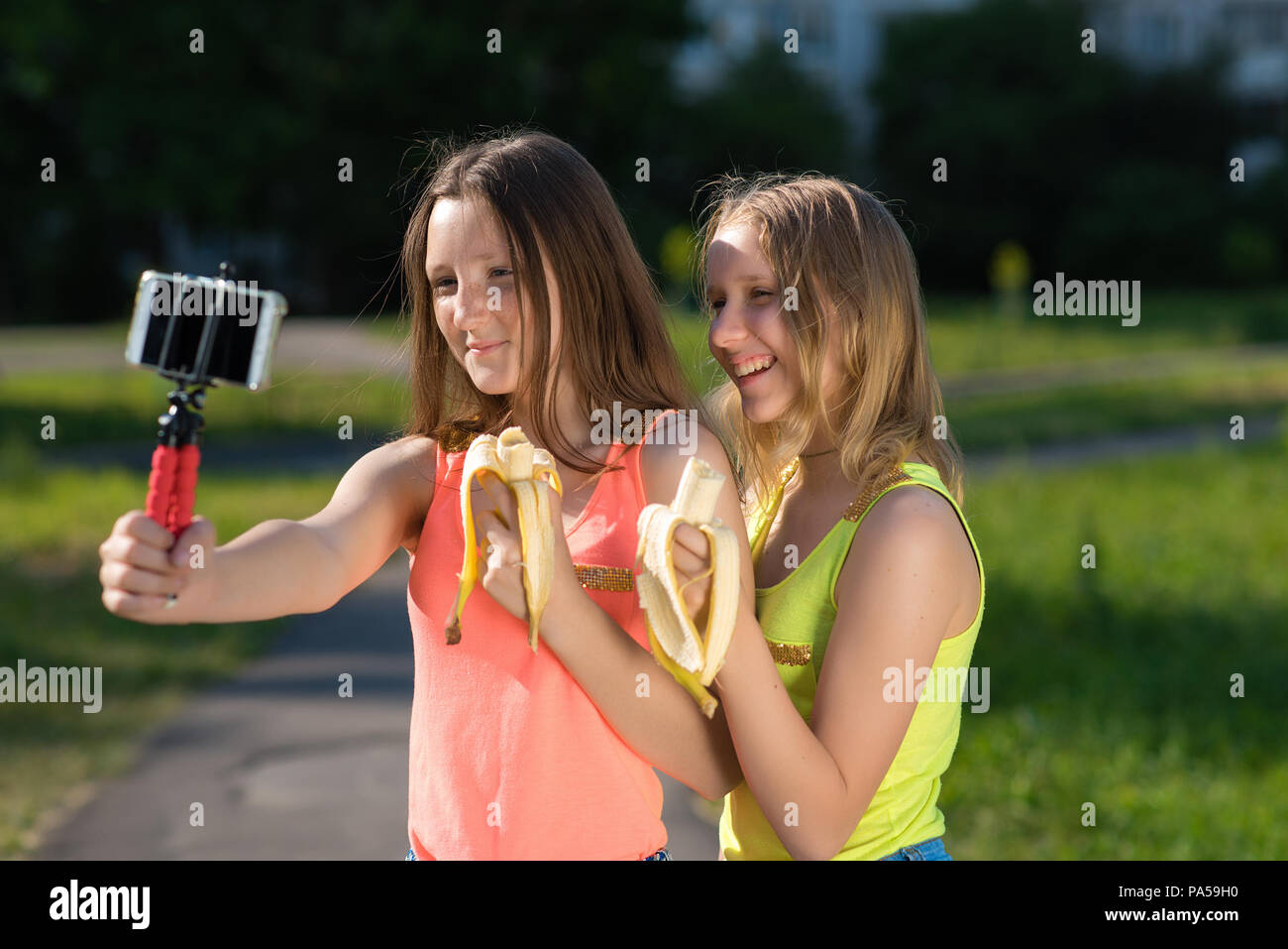 Zwei Mädchen Freundin, in einem Park in der Natur. In den Händen halten, Bananen. Videos auf dem Smartphone. Gefühle von Freude und Vergnügen. Das Konzept der Stockfoto