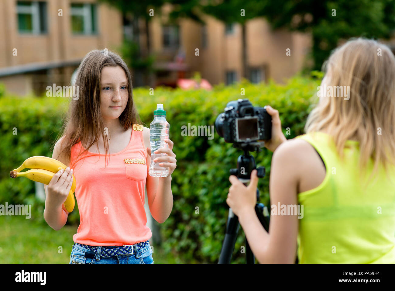 Junge Mädchen Blogger, im Sommer in der Stadt auf die Natur. Video auf der Kamera aufgezeichnet werden. In ihren Händen hält eine Flasche Wasser und zwei Bananen. Verwenden der Kamera wi Stockfoto