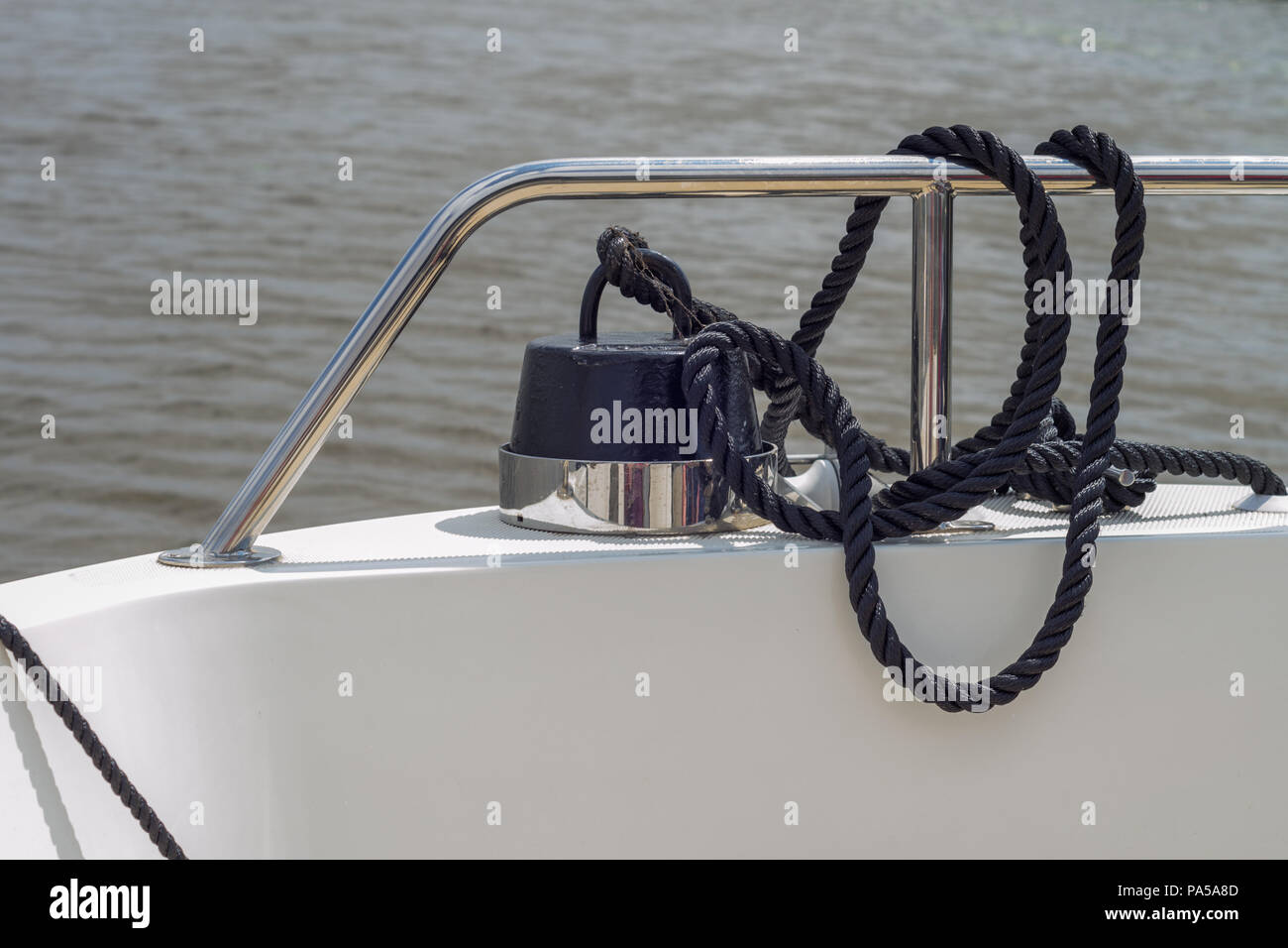 Ein schwarzes Seil zu einem Gewicht gebunden auf einem Boot befestigt, um das Metall Geländer Stockfoto