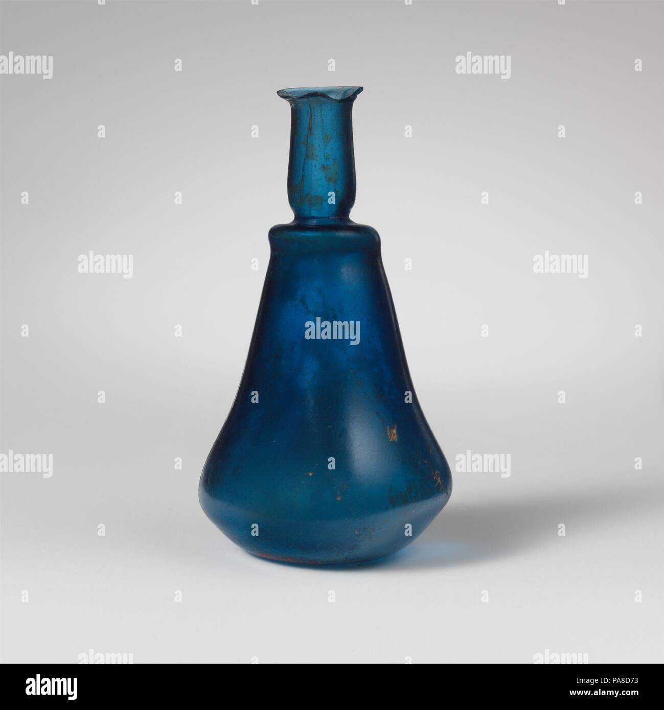 Glas carinated Parfüm Flasche. Kultur: Roman. Abmessungen: H, D, 9.2Cm 4.6cm (Rim, 1,6Cm). Datum: 1. Jh. N.CHR.. Transluzente Kobaltblau. Outsplayed, abgerundete Kante; zylindrische Hals, mit tiefen horizontalen werkzeuggestützte Gedankenstrich um Base; schmalen horizontalen Schulter mit vorgezogener Flansch unten; carinated Körper, mit leicht konkaven Profil an der oberen und unteren Abschnitt geschwungene scharf unten konkav. Intakt, außer um Rim, von denen 2/3 fehlt; einige Blasen, im Hals gestreckt; Mattierung, Patches von Lochfraß und irisierenden Bewitterung im Außenbereich, weißlich Überstehen auf viel Innenraum. Stockfoto