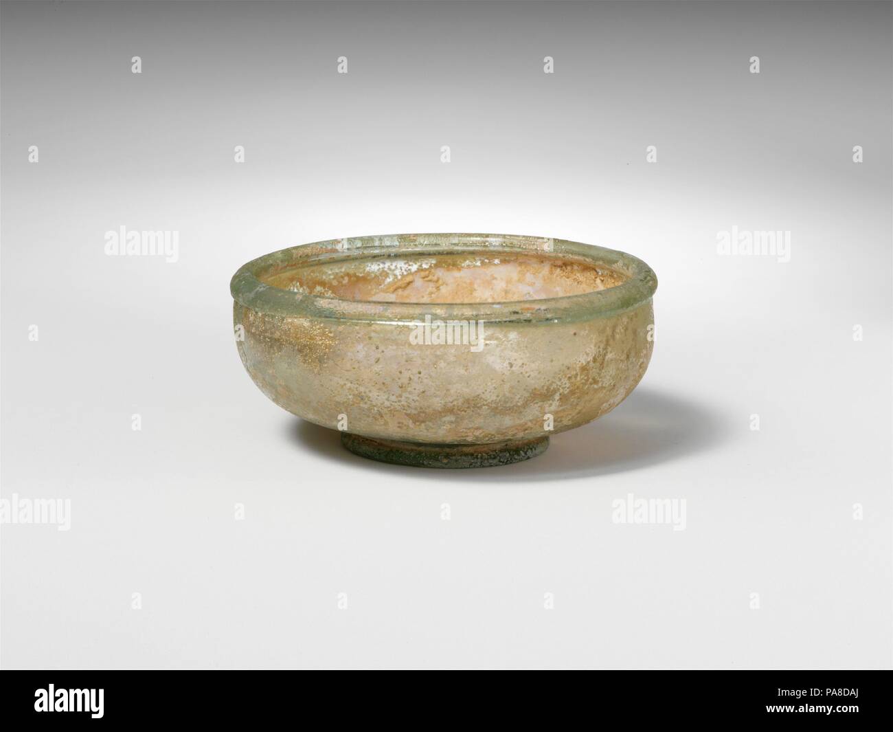 Glasschale. Kultur: Roman. Abmessungen: Insgesamt: 1 1/4 x 2 7/8 x 1 3/8 in. (3,2 x 7,3 x 3,5 cm). Datum: Ca. 3. Jahrhundert n. Chr.. Farblos mit hellen grünliche Färbung. Dick, abgerundete Kante, die innere Lippe; kurz, konvex, geschwungenen Seiten zu Körper; solides pad Base; mit flachem Boden, mit kleinen Kick in der Mitte und pontil markieren. Intakt; viele Pinprick blasen; Lochfraß, Mattieren, und irisierenden Bewitterung im Außenbereich, leichte Böden Verkrustung und cremig Braun überstehen auf Interieur. Museum: Metropolitan Museum of Art, New York, USA. Stockfoto