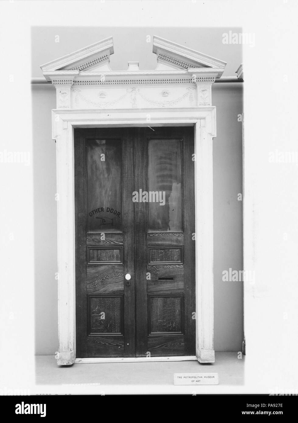 Eingang. Kultur: American. Abmessungen: 120 x 69 in. (304,8 x 175,3 cm). Datum: Ca. 1800. Das Design dieser Tür und die Dekoration sind charakteristisch für Philadelphia Architektur der frühen Bundesrepublik. Die Tür verfügt über eine gebrochene Giebel und ein Fries mit angewandte Komposition Ornamenten verziert ist. Details der Frieze gehört ein drapiert klassische Figur, in der Mitte und hält eine Girlande in jedem erhobenen Hand. Museum: Metropolitan Museum of Art, New York, USA. Stockfoto