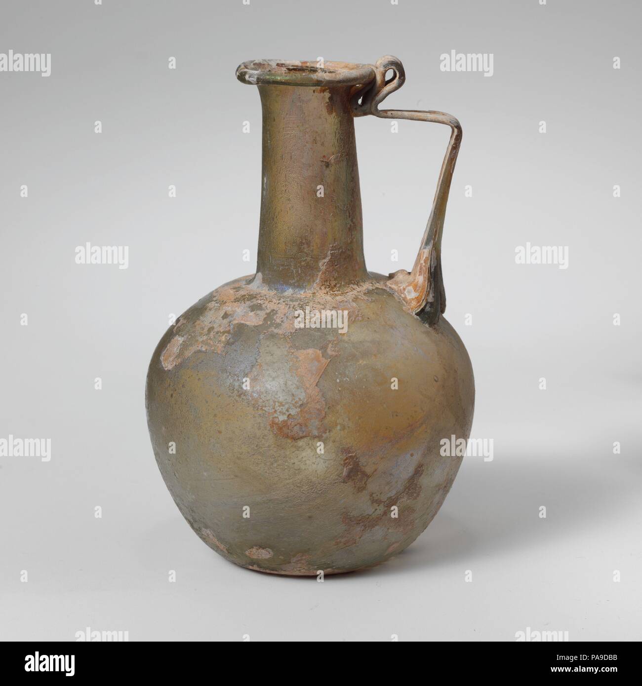 Glaskanne. Kultur: Roman. Abmessungen: 4 1/8 in. (10,5 cm) Andere: 2 3/4 in. (7 cm) Durchm. Von rim: 1 1/8 in. (2,8 cm). Datum: 2.-3.Jh. N.CHR.. Durchsichtig gelb grün; in der gleichen Farbe. Rim gefaltet ungleichmäßig aus, rund, und in; leicht trichterförmig zylindrische Hals, mit schnittspuren an der Basis; kugelförmigen Körper; konkave Unterseite; Strap Griff in drei Dicken kralle Pads an Schulter, erarbeitet und in horizontal gedreht, mit einem doppelten vertikalen als Daumen oben rim Falten, und dann brach auf von Hals- und Außenrand der Felge nach oben. Intakt; viele Blasen; Mattierung, Lochfraß, und ich Stockfoto