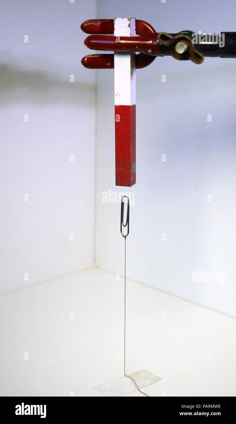 Eine Büroklammer, um eine Tabelle mit einer roten Schnur schwebt unter einem Magnet., Stockfoto