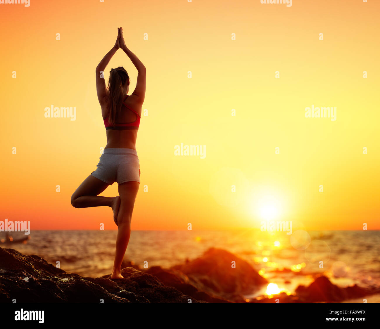 Yoga bei Sonnenuntergang - Mädchen in Vrikshasana darstellen Stockfoto