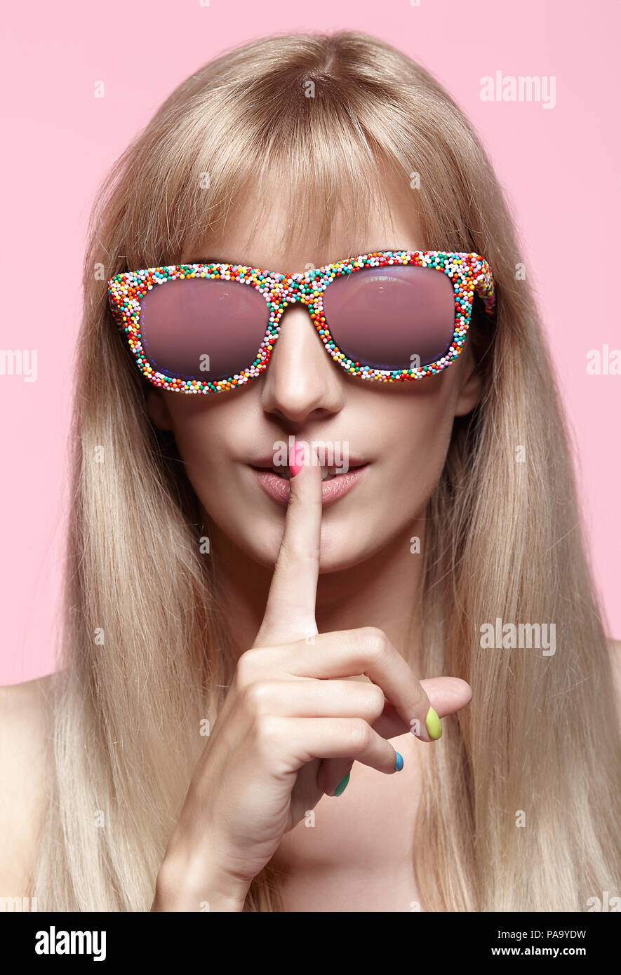 Junge blonde Frau mit Spaß Süßigkeiten Gläser auf rosa Hintergrund. Porträt von Frauen mit den Finger auf die Lippen Stockfoto