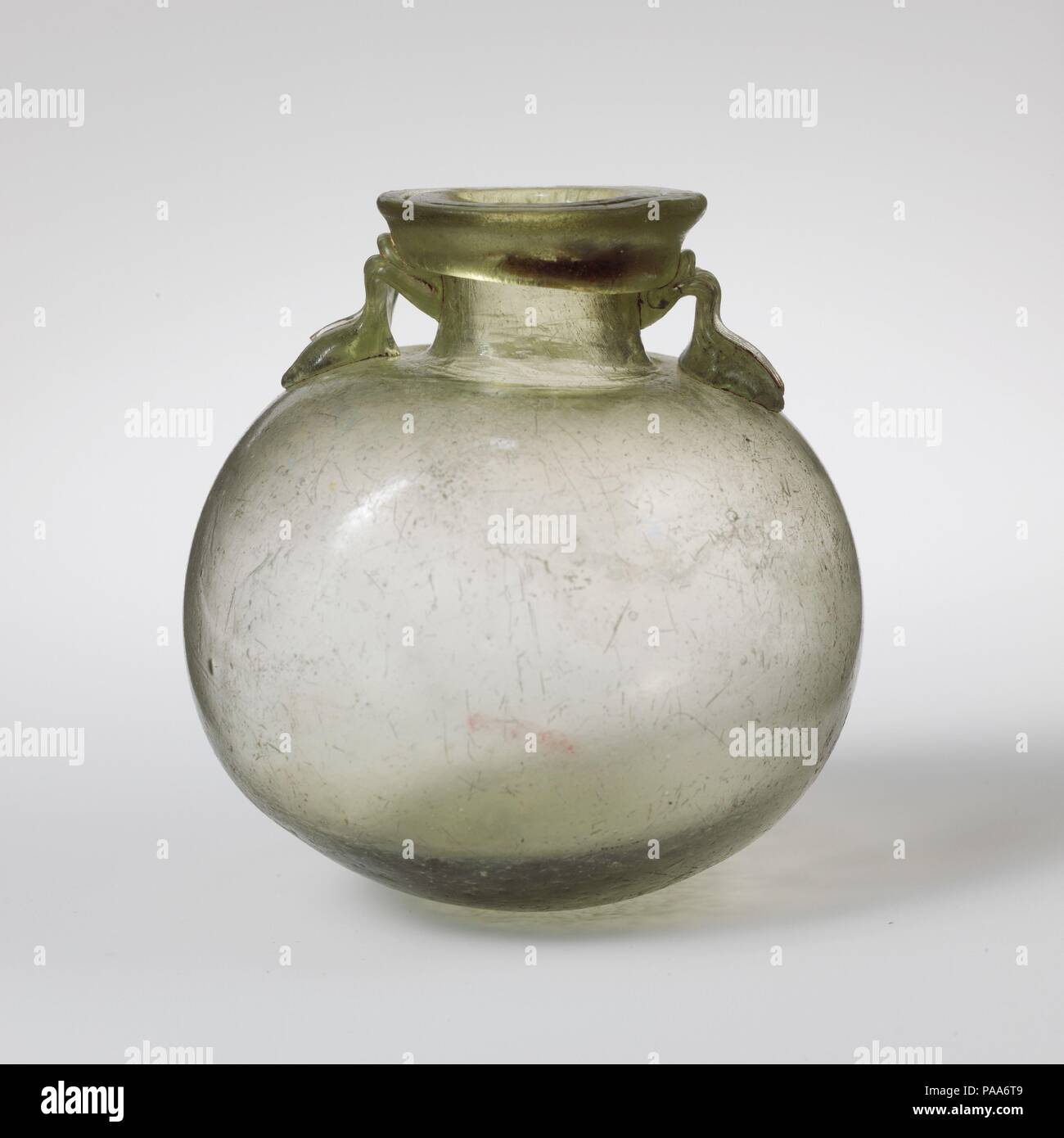 Glas aryballos (Öl Flasche). Kultur: Roman, im östlichen Mittelmeer. Abmessungen: H.: 3 1/16-in. (7,8 cm). Datum: 1.-3.Jh. N.CHR.. Transluzente blass grün; Griffe in der gleichen Farbe. Collared rim ausgeklappt, unten, rund, und up, und flach auf die Oberseite, mit hervorstehenden äußeren Flansch; kurz zylindrischen Hals kugelförmigen Körper; runden Boden; zwei kleine Griffe angewendet wird der Körper in runde Pads, erarbeitet und schleppte am Hals und an der Unterseite von RIM. Intakt; einige Blasen und ein Paar schwarze Verunreinigungen, mit Löcher und Kratzer auf der Unterseite; ein Patch von Lochfraß auf Körper, und Schwache irisierende Wetter Stockfoto