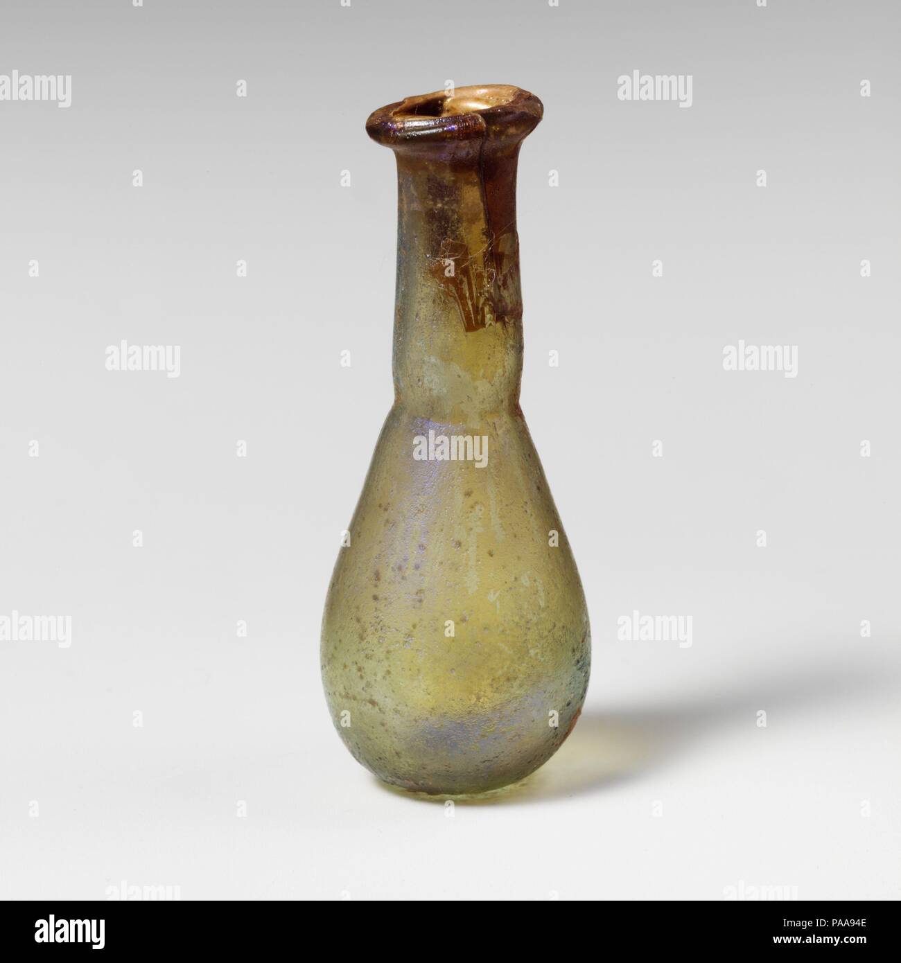 Glas Parfüm Flasche. Kultur: Roman. Abmessungen: Höhe: 2 3/16 in. (5,5 cm) Durchmesser: 7/8 x 5/8 in. (2,2 x 1,6 cm). Datum: 1. Jh. N.CHR.. Kleine Parfumflasche Farblos mit hellen blau-grüne Färbung. Ungleichmäßige, lop-seitig Rim, gefaltet, über, und in; zylindrische Hals, Erweiterung leicht nach unten und werkzeuggestützte in um Base; piriform Körper, runder Boden, in der Mitte abgeflacht. Intakt, aber Riss in Rim und Hals; viele pinprick und kleine Blasen; Mattierung und schwache Schillern, mit Patch von dicken, cremigen, Emaille - wie Verwitterung auf Felge und oben am Hals. Museum: Metropolitan Museum of Art, New York, U Stockfoto
