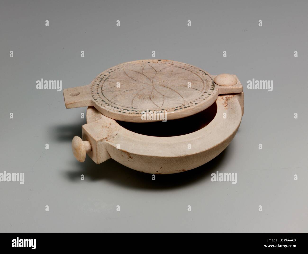 Kosmetik Box mit einem drehbaren Oberteil. Abmessungen: L 9,2 cm (3 5/8 in.); W. 7,7 cm (3 1/16 in.); H. 2.5cm (1 5/16 in.). Dynastie: Dynasty 18, früh. Datum: Ca. 1550-1458 v. Chr.. Dieses kleine Elfenbein Box hat einen Deckel, der an einem Ende gekoppelt ist, so dass es offen zu schwenken und geschlossen. Das Loch am anderen Ende der Deckel hielt einmal einen anderen Peg. Wenn geschlossen, die Peg in den Deckel, und stellen Sie den PEG ragen aus der Box könnte zusammen mit String die Box aus der Öffnung zu halten gebunden werden. Die Oberseite der Box hat mit eingeschnittenen Linien, eine Rosette, umrahmt von einem zig-zag Muster Formular eingerichtet. Die Rosette wurde wahrscheinlich benötigten Stockfoto