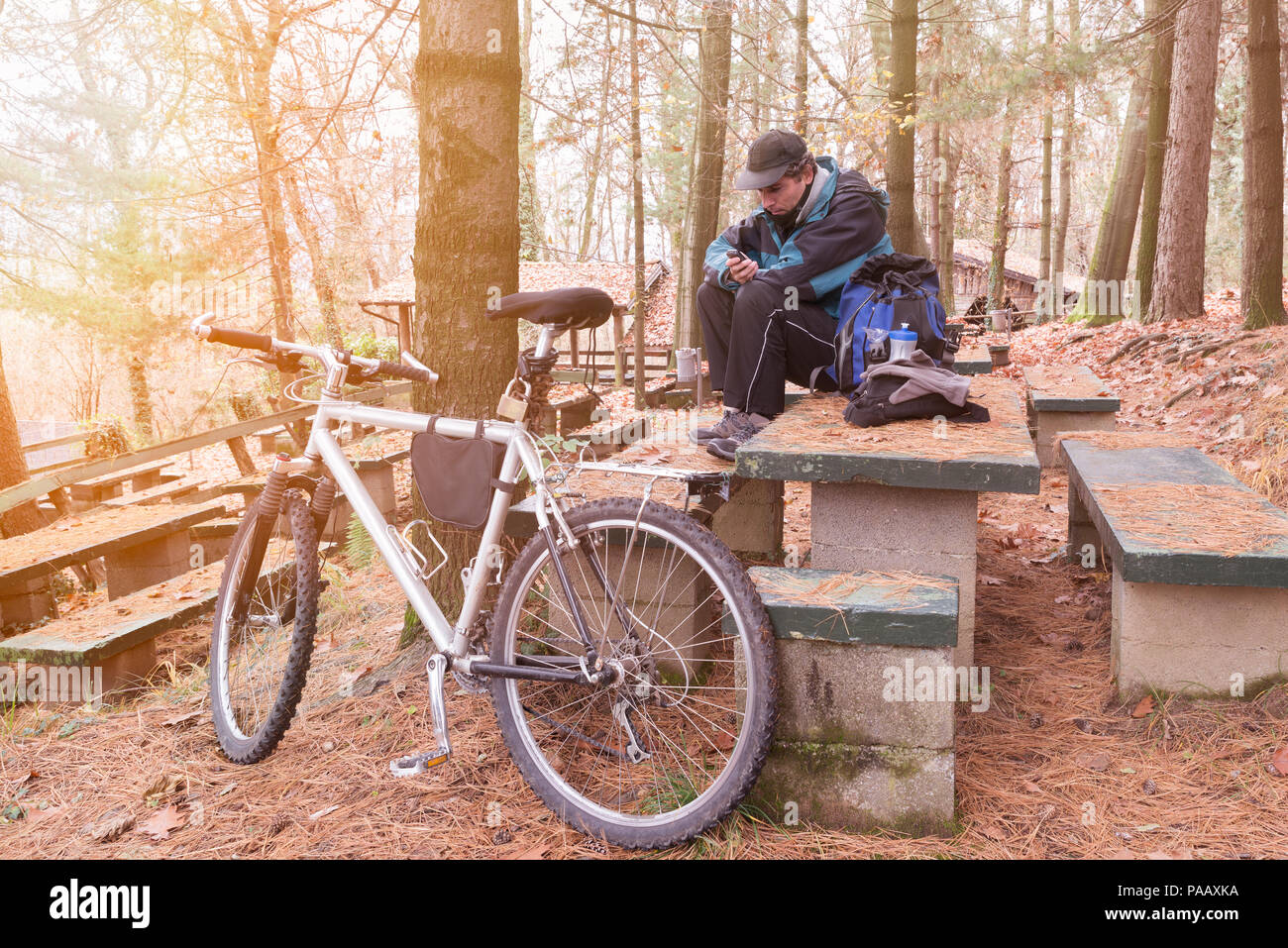Radfahrer mit Mountainbike und cellphone ruht auf einem picknickplatz an einem kalten Wintermorgen. Sport und Aktivitäten im Freien in der Natur Stockfoto