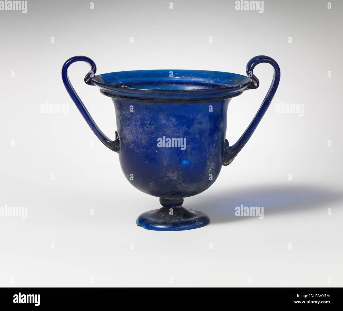 Glas cantharus (Trinkbecher). Kultur: Roman. Abmessungen: H.4 11/16 in. (11,9 cm). Datum: Ca. Chr. 40-80. Transluzente kobalt blau; Griffe in der gleichen Farbe. Abfackeln, abgerundete Kante, mit gefalteten solide Flansch unten; glockenförmige Körper, Carving in scharf zu festen, kurzen Stiel; niedrig, gespreizter Fuß, aus einer separaten sammeln mit geklopft und am äußeren Rand gebildet; ungleichmäßige, flacher Boden; Low Kick in der Mitte der Innenseite des Körpers; strap Handles angefügten Seiten des Körpers in Pads zu senken, WERKZEUGGESTÜTZTE Wohnung über, erarbeitet und nach außen gewölbten runden und dann in einer Schleife über Rim und wirkt auf die Lippe und die Unterseite des Stockfoto