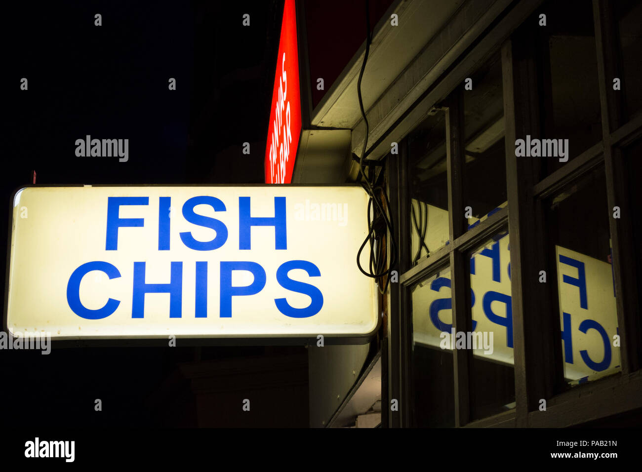 Eine beleuchtete Fish und Chips Zeichen außerhalb einen Fisch und Chip Shop in London, Großbritannien Stockfoto