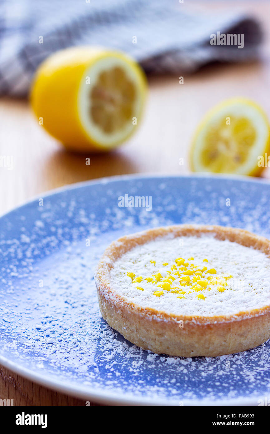 Eine kleine Lemon tart auf einem Teller mit frischer Zitrone im Hintergrund. Stockfoto