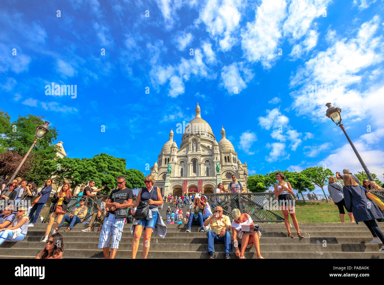 Paris, Frankreich, 3. Juli 2017: Viele Leute auf der Treppe der Basilika Sacré Coeur de Montmartre in Paris an einem sonnigen Tag mit blauen Himmel. Herz-jesu-Kirche ist eine beliebte touristische Sehenswürdigkeit. Ansicht von unten. Stockfoto
