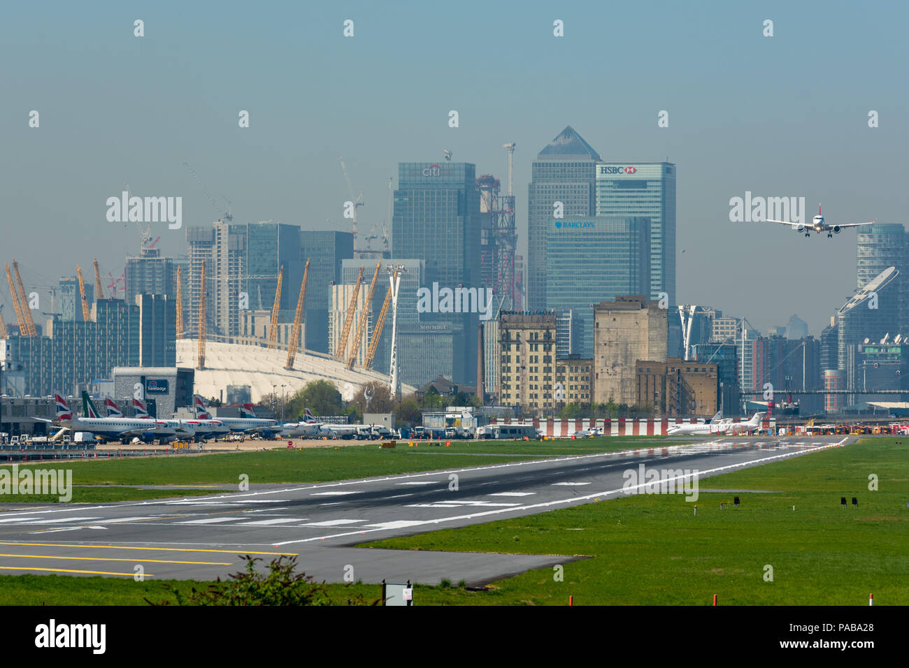 Airbus A 220-100 auf Final Approach in London City Airport, mit den Türmen der Canary Wharf Financial District und die O2 im Hintergrund Stockfoto