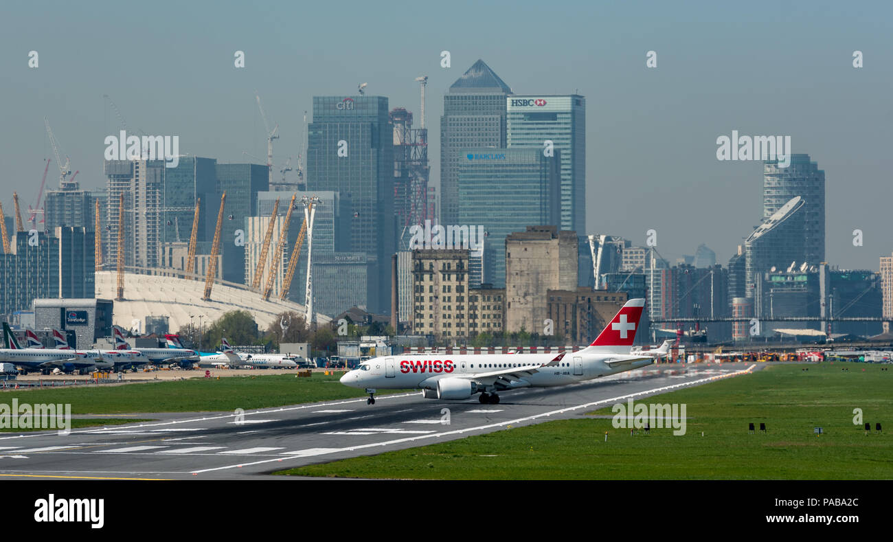 Eine neu eingetroffenen Airbus A 220-100 rollens am London City Airport, mit den Türmen von Canary Wharf und die O2 im Hintergrund Stockfoto