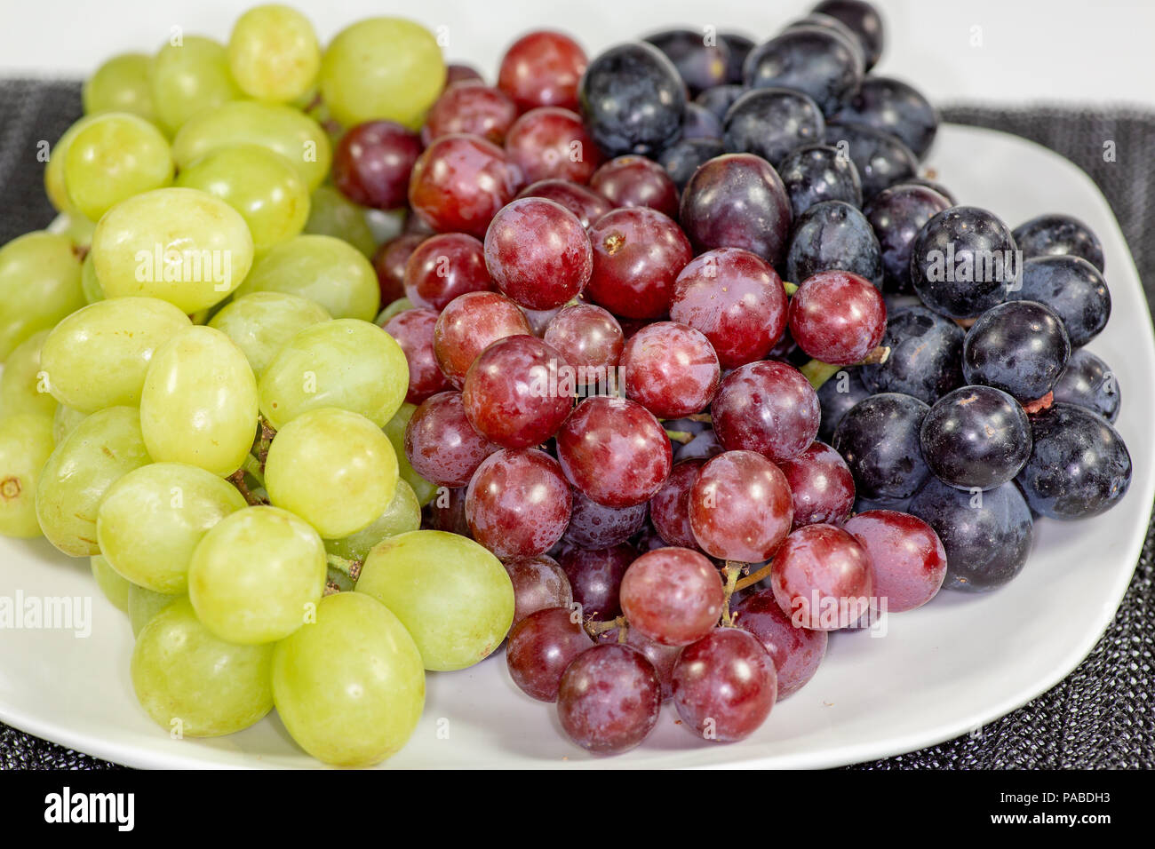 Schwarz, Rot, Grün kernlose Trauben in einer tiefen weiße Schüssel auf einem weißen Geschichte warten auf Frühstück gegessen zu werden. Stockfoto