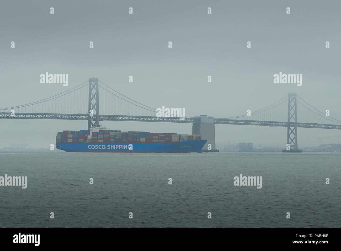 COSCO SHIPPING Container Ship, CSCL BOHAI SEA verlässt Oakland und unterquert die San Francisco-Oakland Bay Bridge am frühen Morgen im Sea Mist. Stockfoto